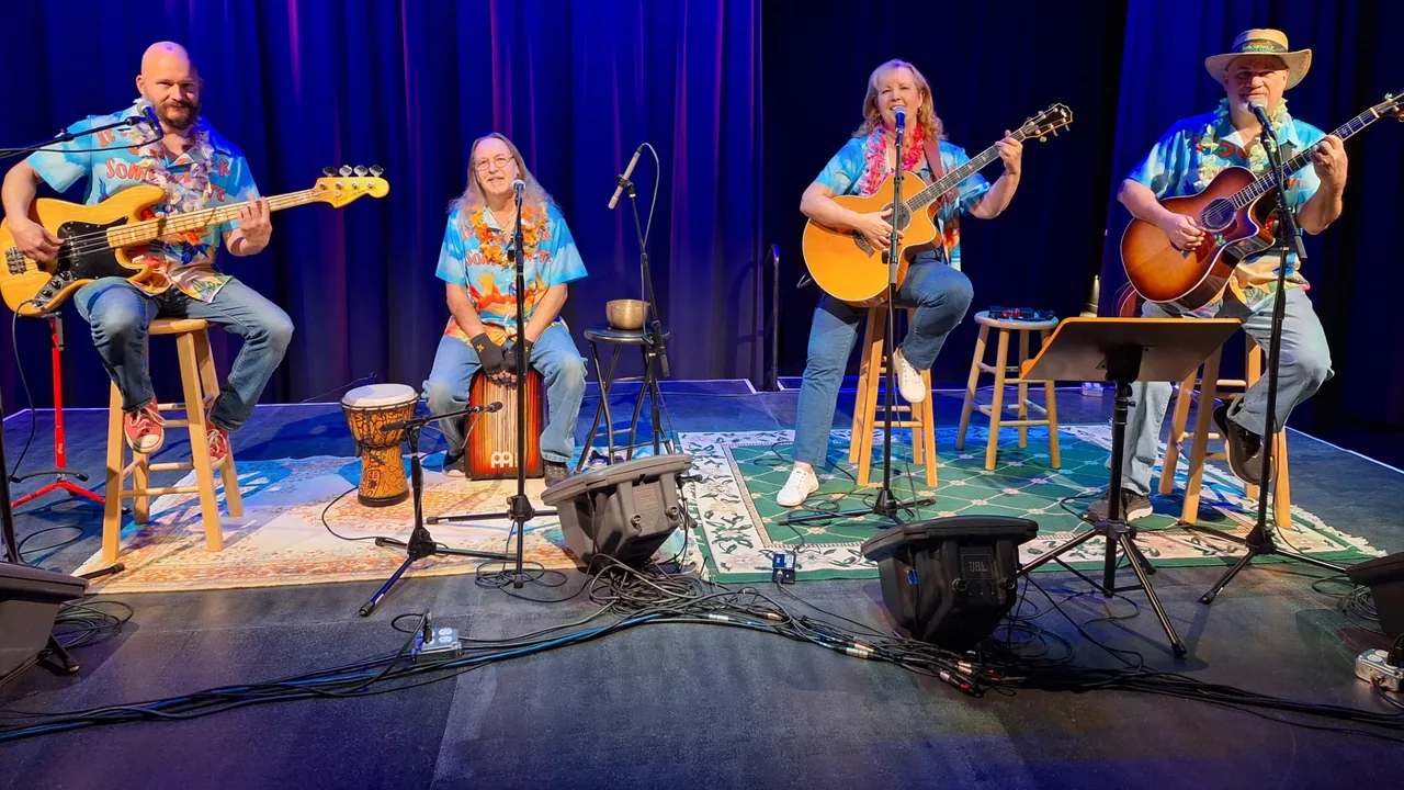 Four musicians in Hawaiian shirts play guitars and drums on a small stage.