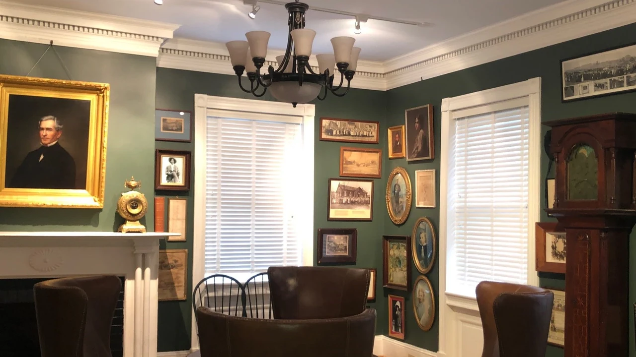 A historic parlor with a portrait over the mantel, framed pictures and leather chairs