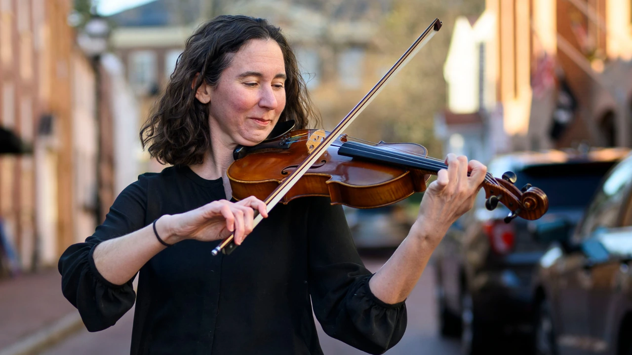A violinist in black plays outdoors on a city street.