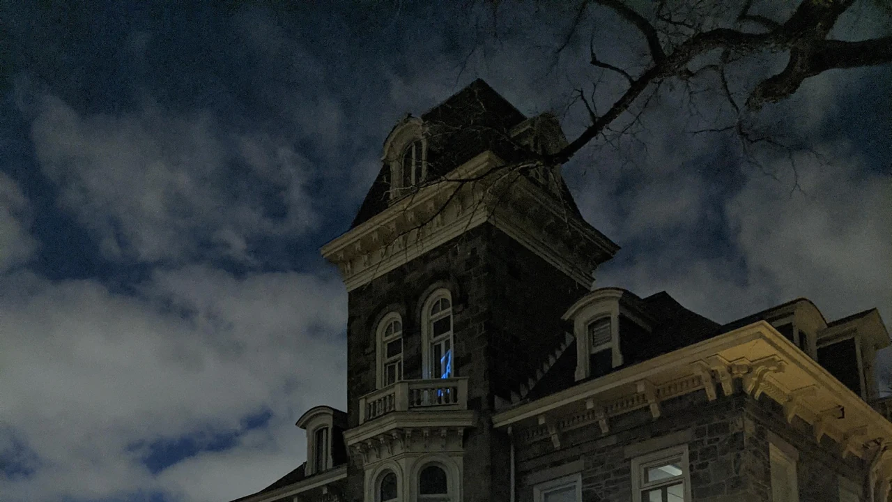 A Victorian stone mansion with a tower under a dark cloudy sky.