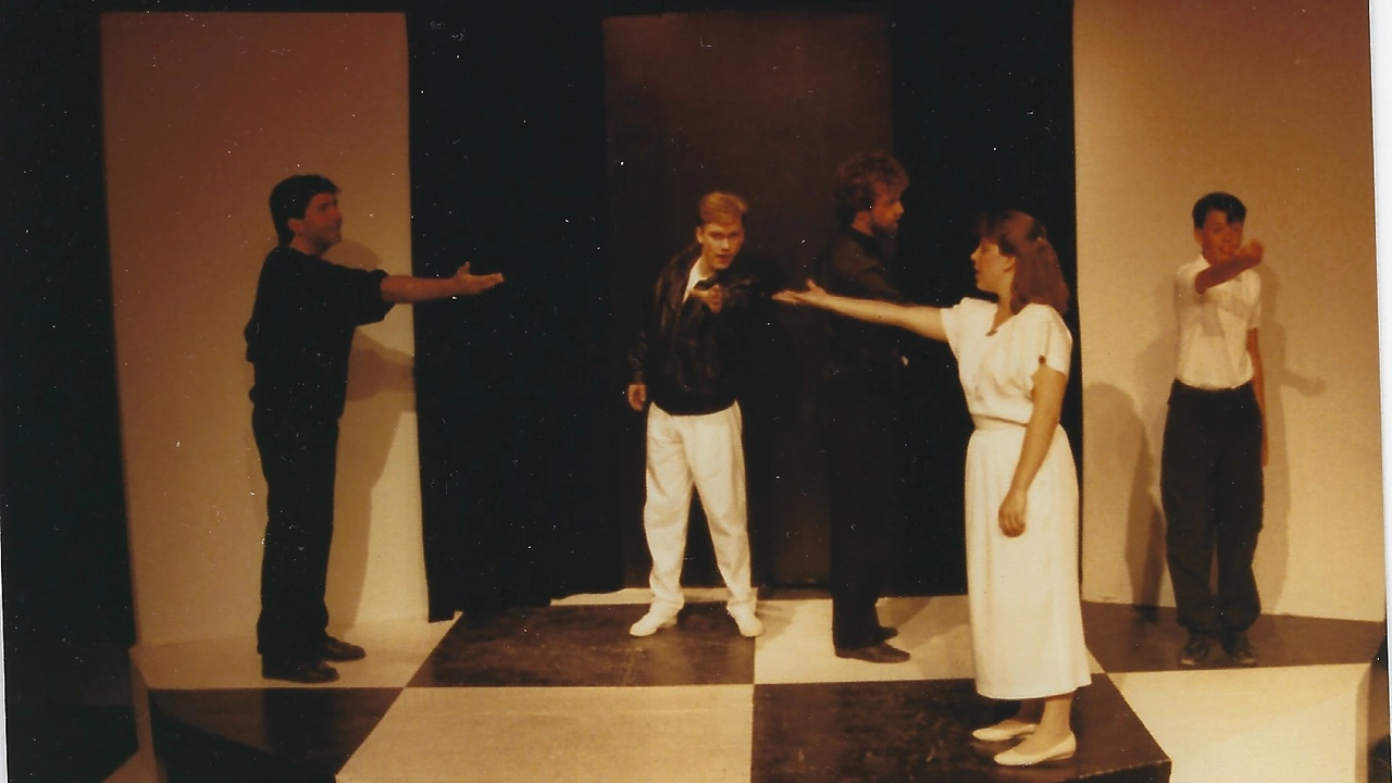 Actors perform a scene on a stage with a black-and-white checkered floor