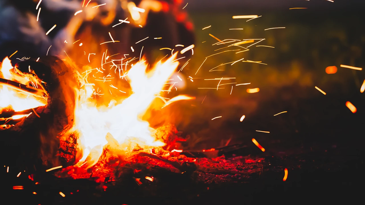 Sparks rise from a crackling campfire at night.
