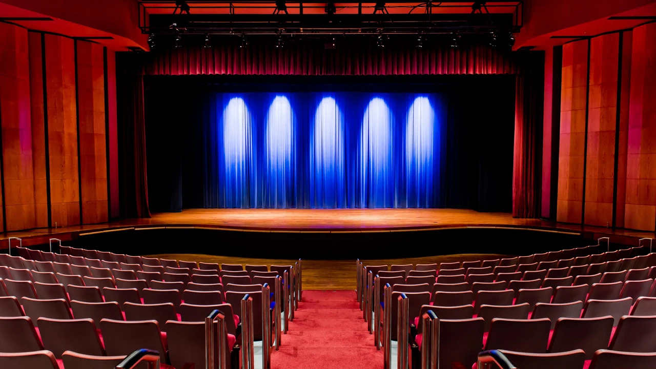An empty theater stage lit in blue with red seats