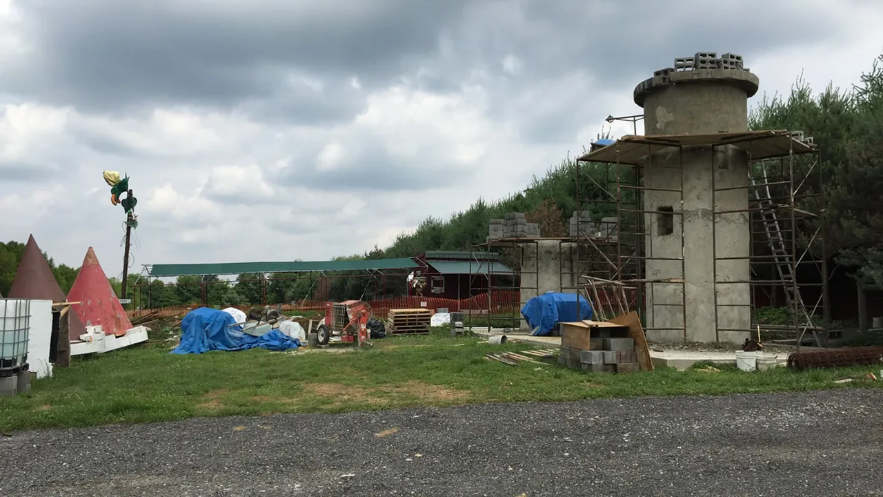 A farm yard with a stone silo tower, red tepees and play structures under a cloudy sky.