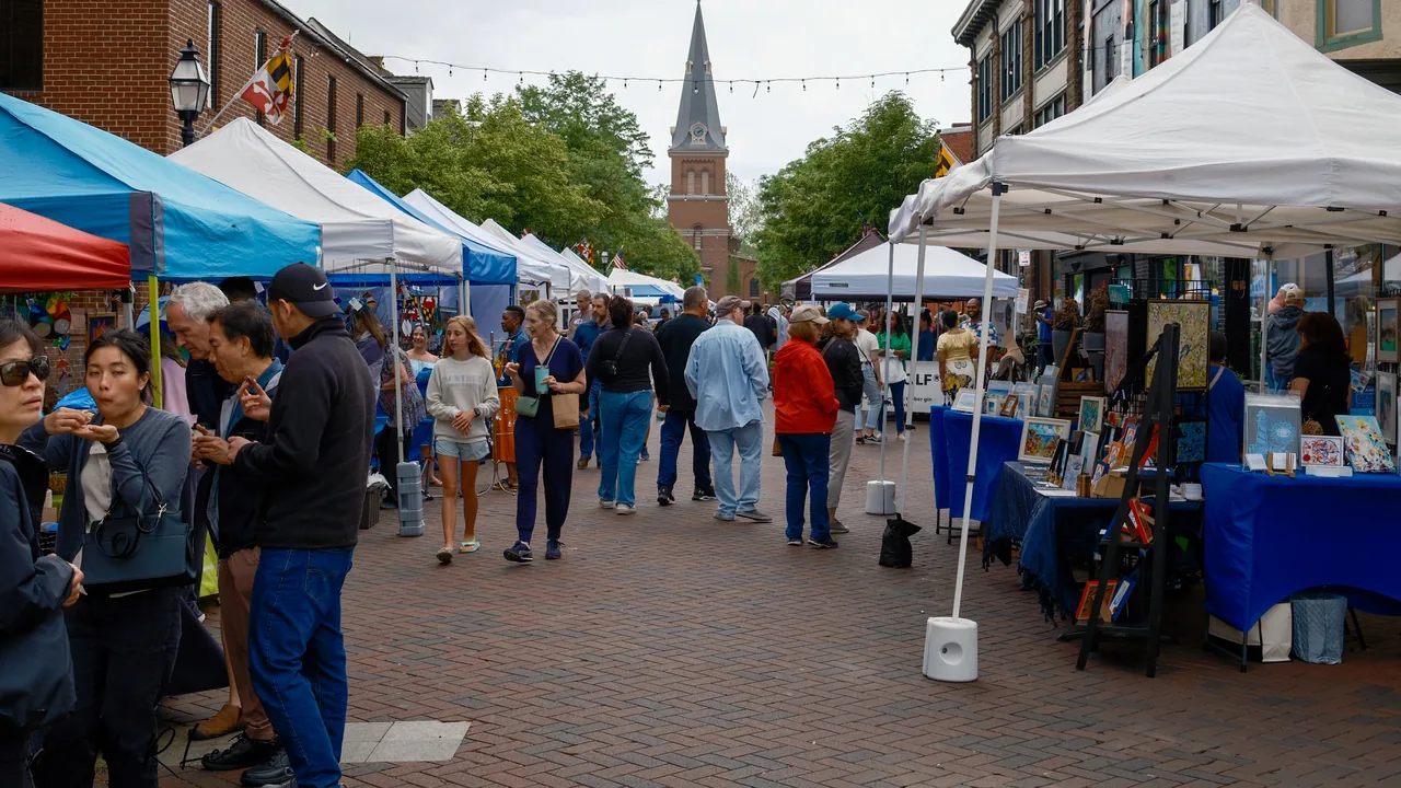 Shoppers stroll a brick street lined with white vendor tents.