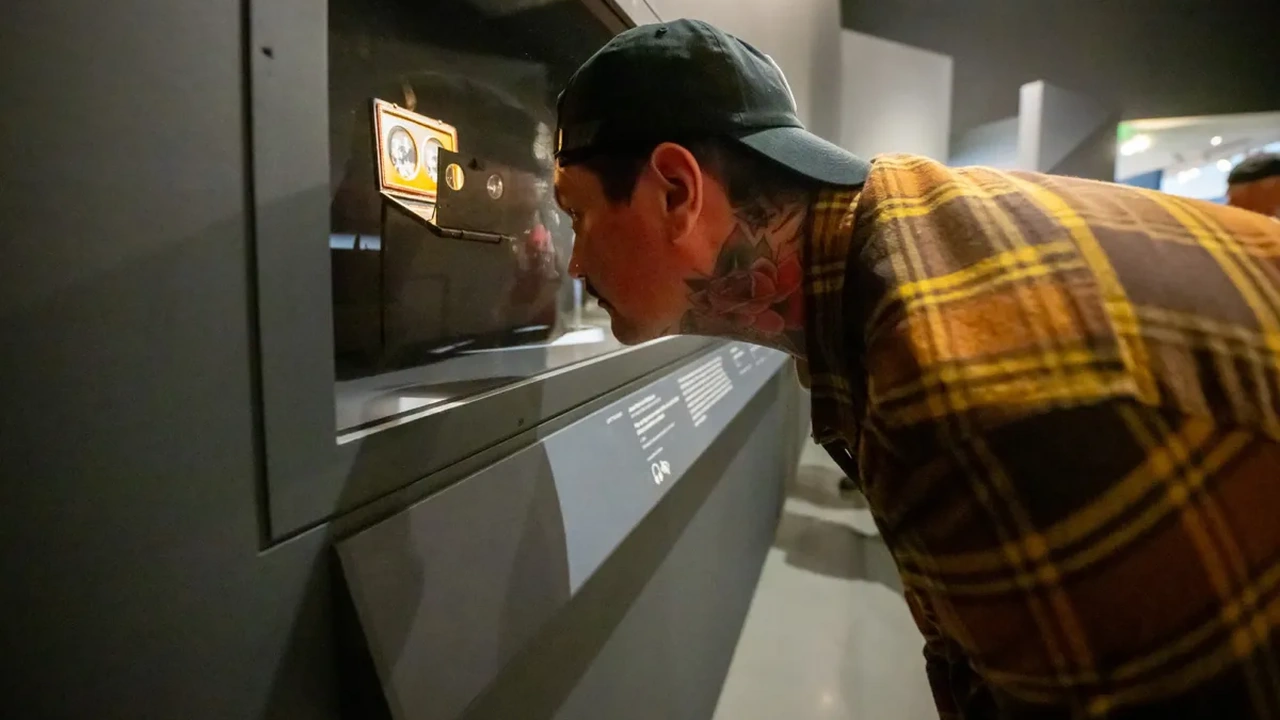 A man in a plaid shirt and cap leans in to look closely into a museum display case.