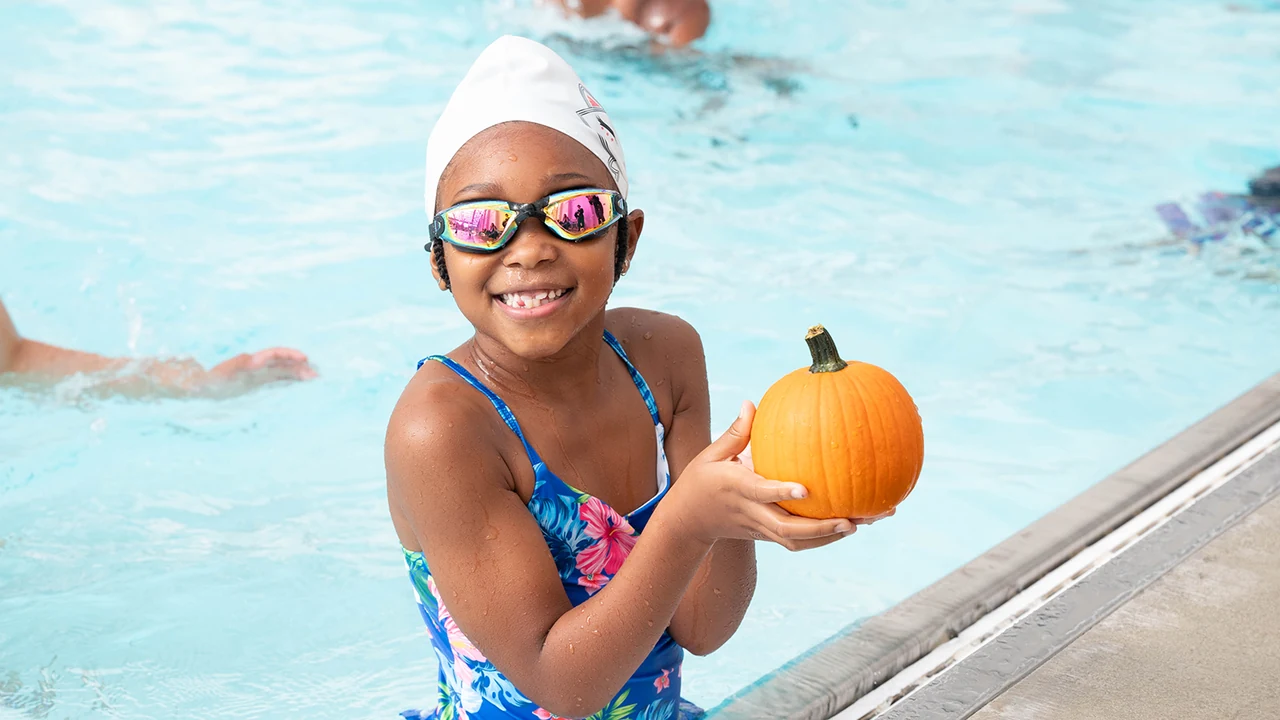 A girl in a pool holds a pumpkin