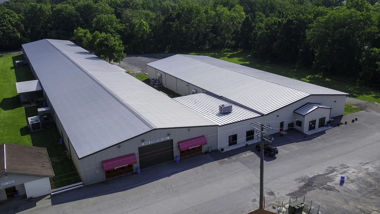 Aerial view of long white exhibition buildings and a parking lot surrounded by trees