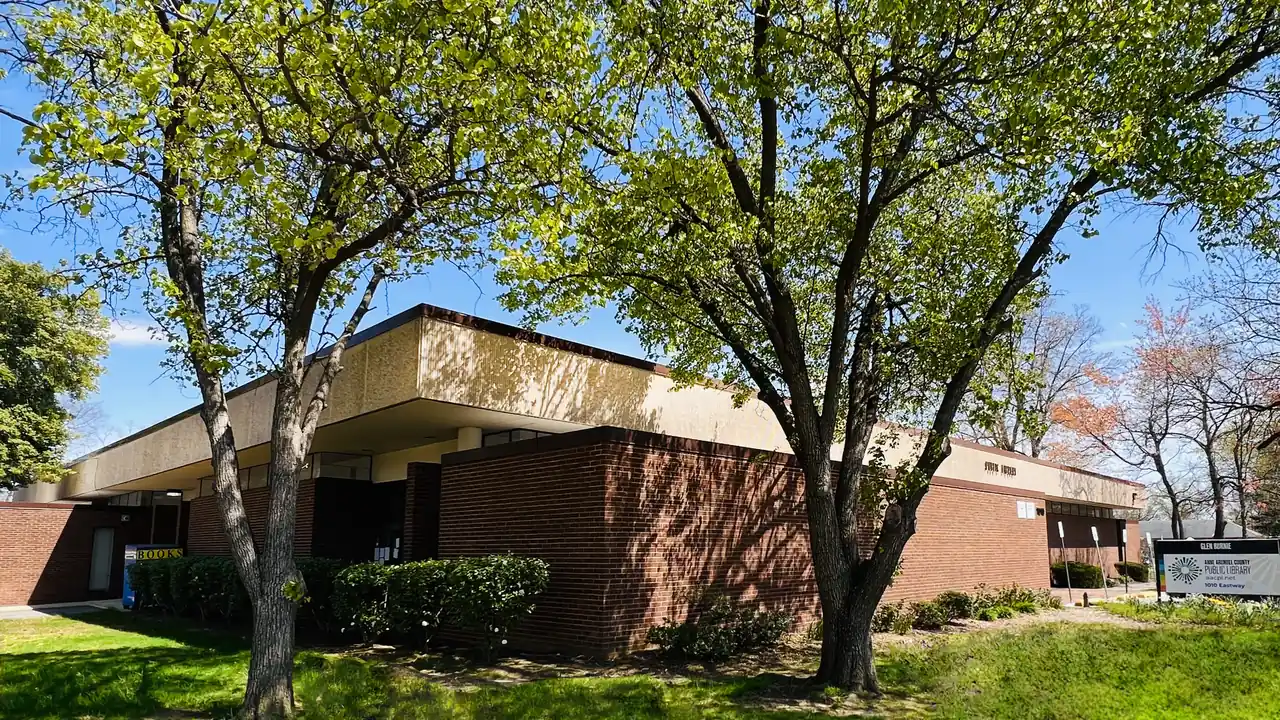 A low brick building with a flat roof behind a lawn and leafy trees.