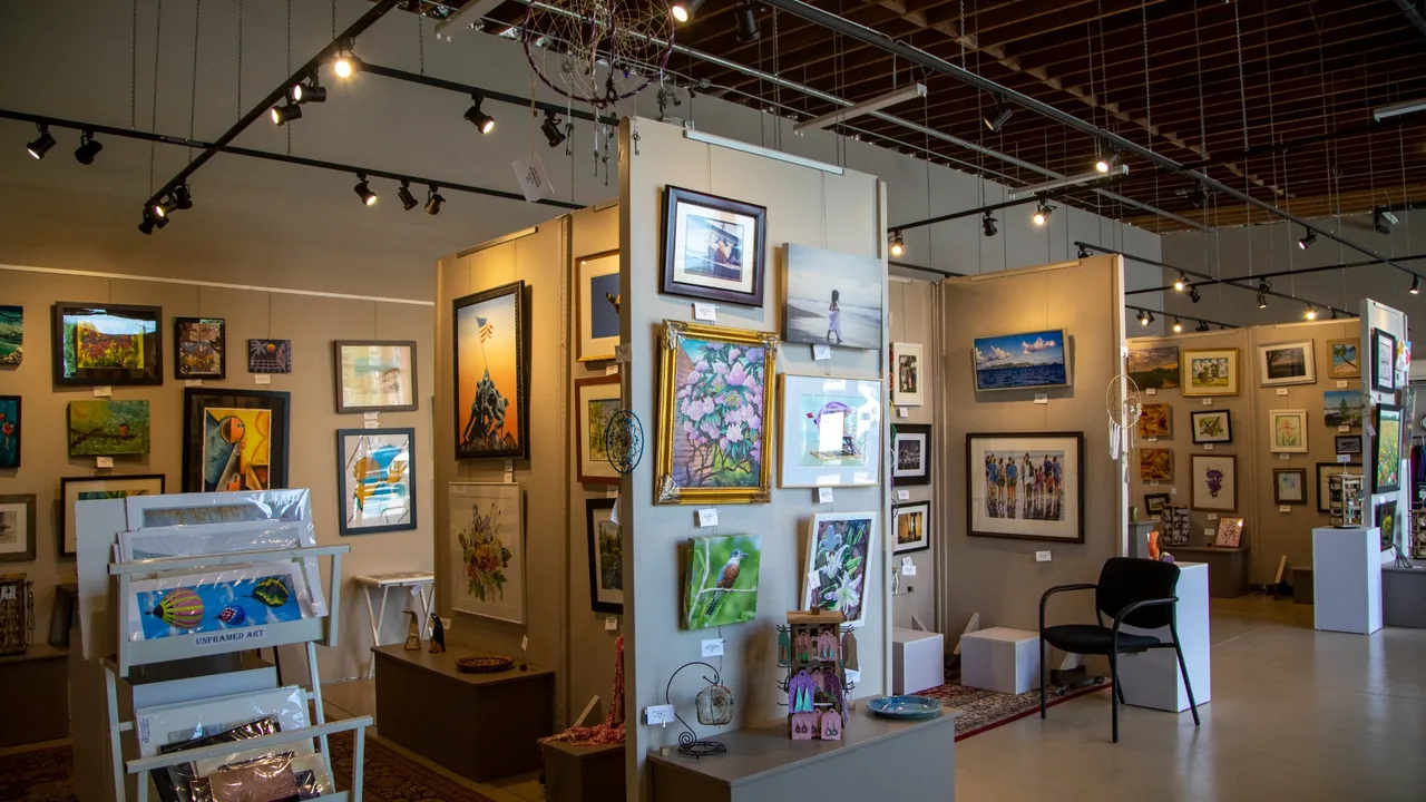 An art gallery room with framed paintings on the walls and a card rack