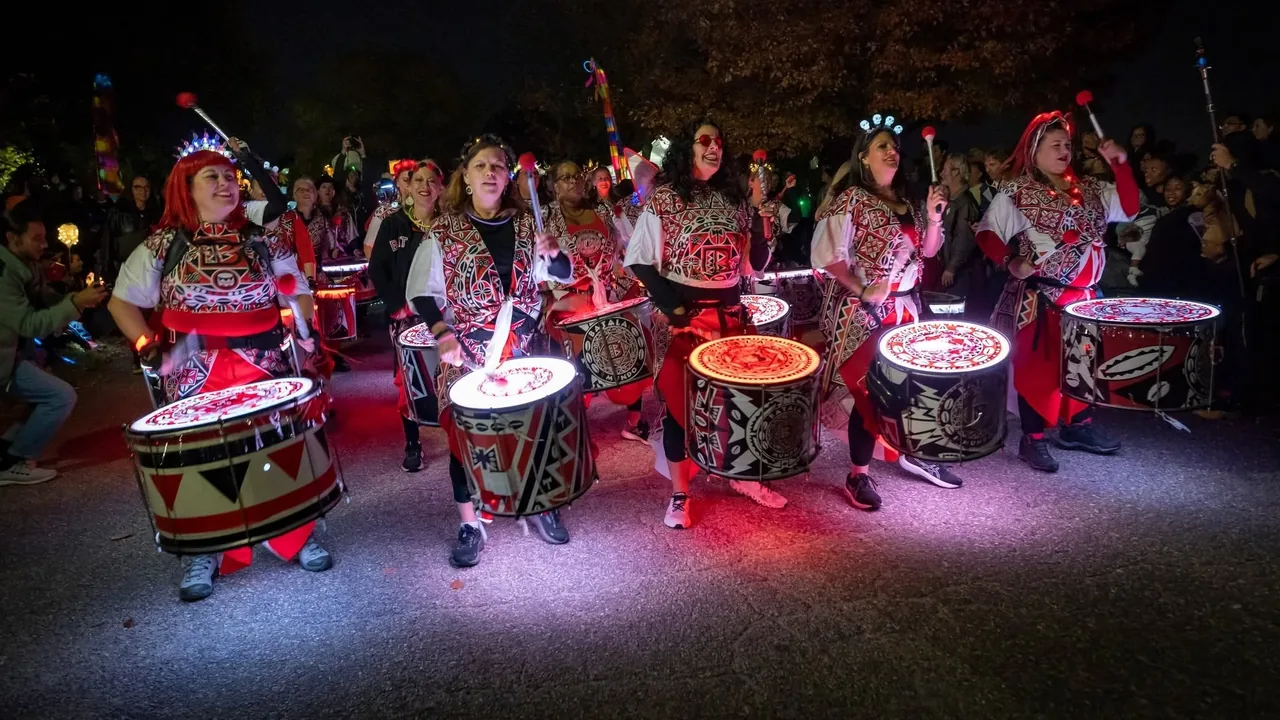 Drummers in bright costumes march with lit drums through a nighttime crowd.