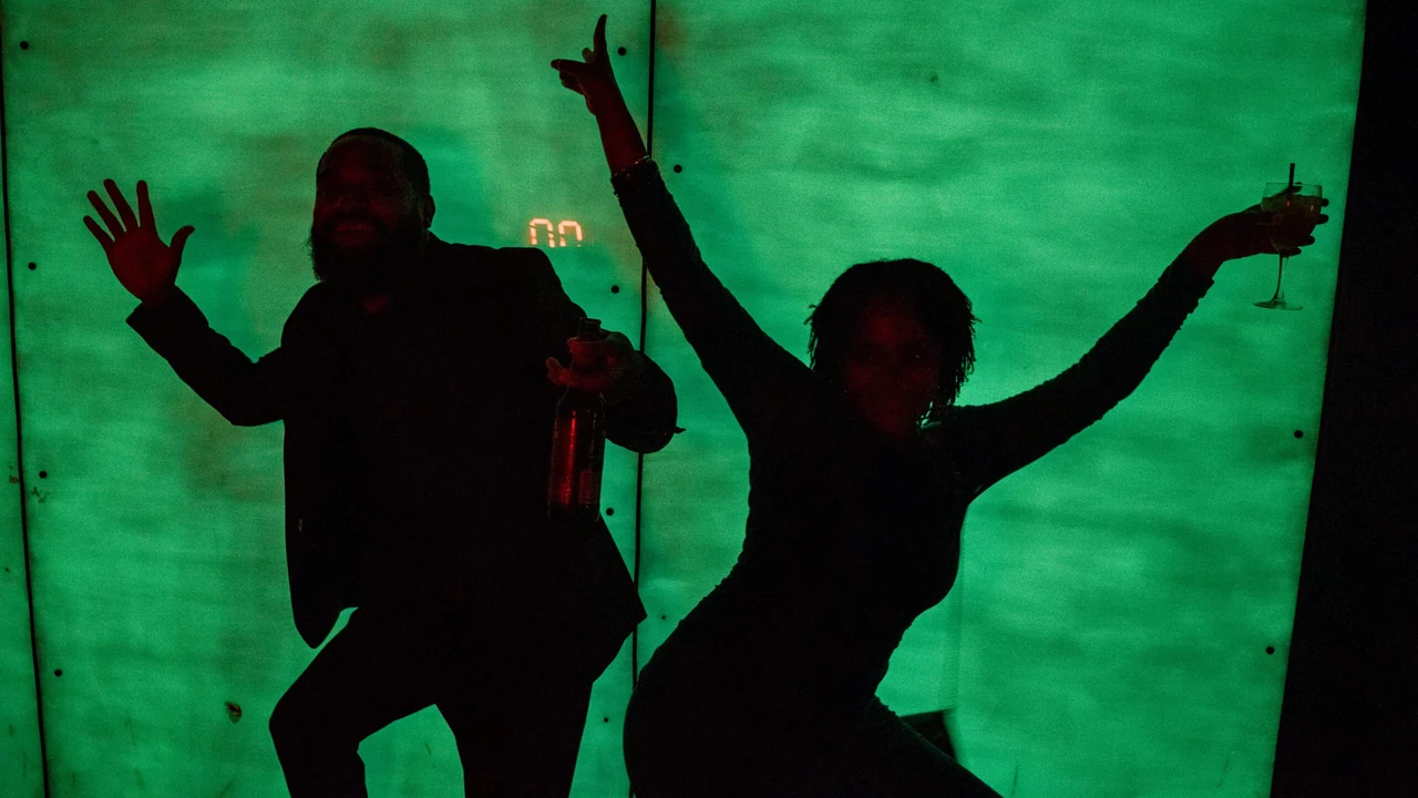 Silhouettes dance against a glowing green wall