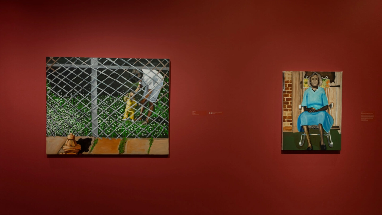 Two paintings, a figure behind a chain-link fence and a seated woman in blue, hang on a deep red gallery wall.