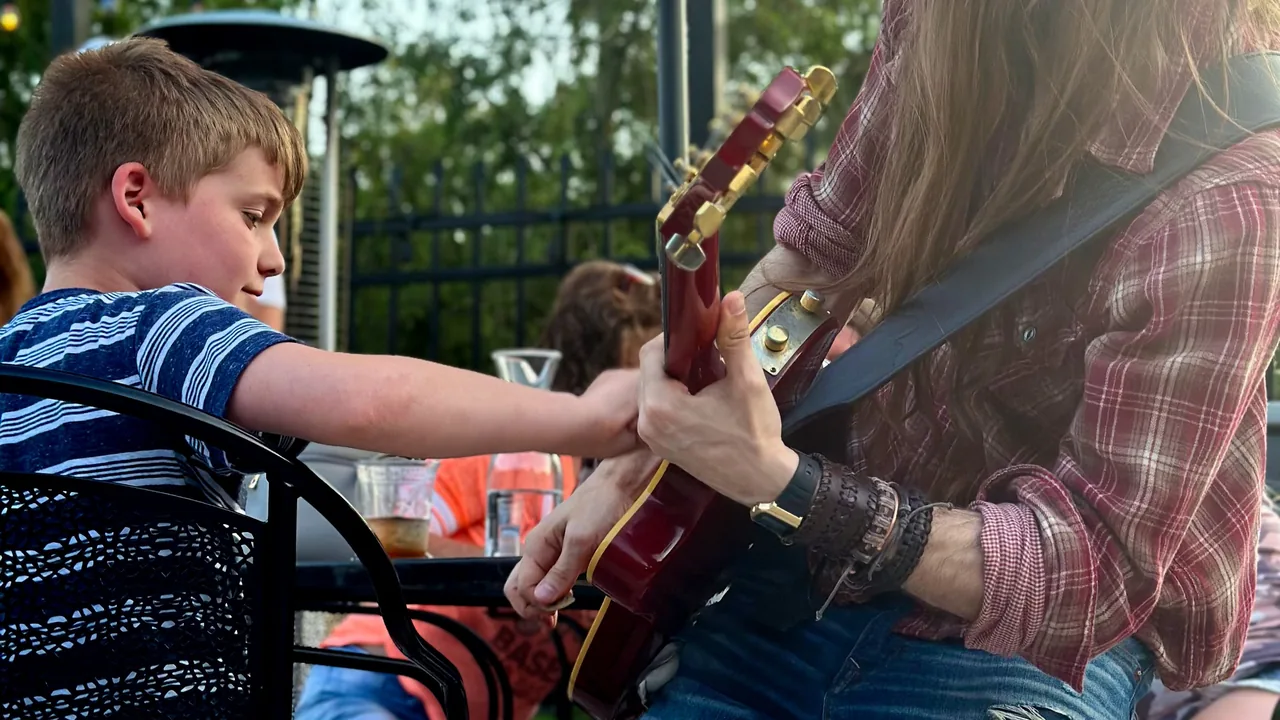 A boy watches a guitarist play outdoors