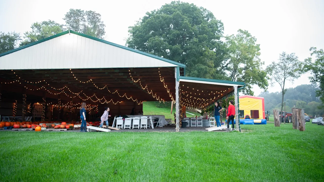 A large open-sided pavilion strung with lights beside a green lawn, with pumpkins and a few visitors.