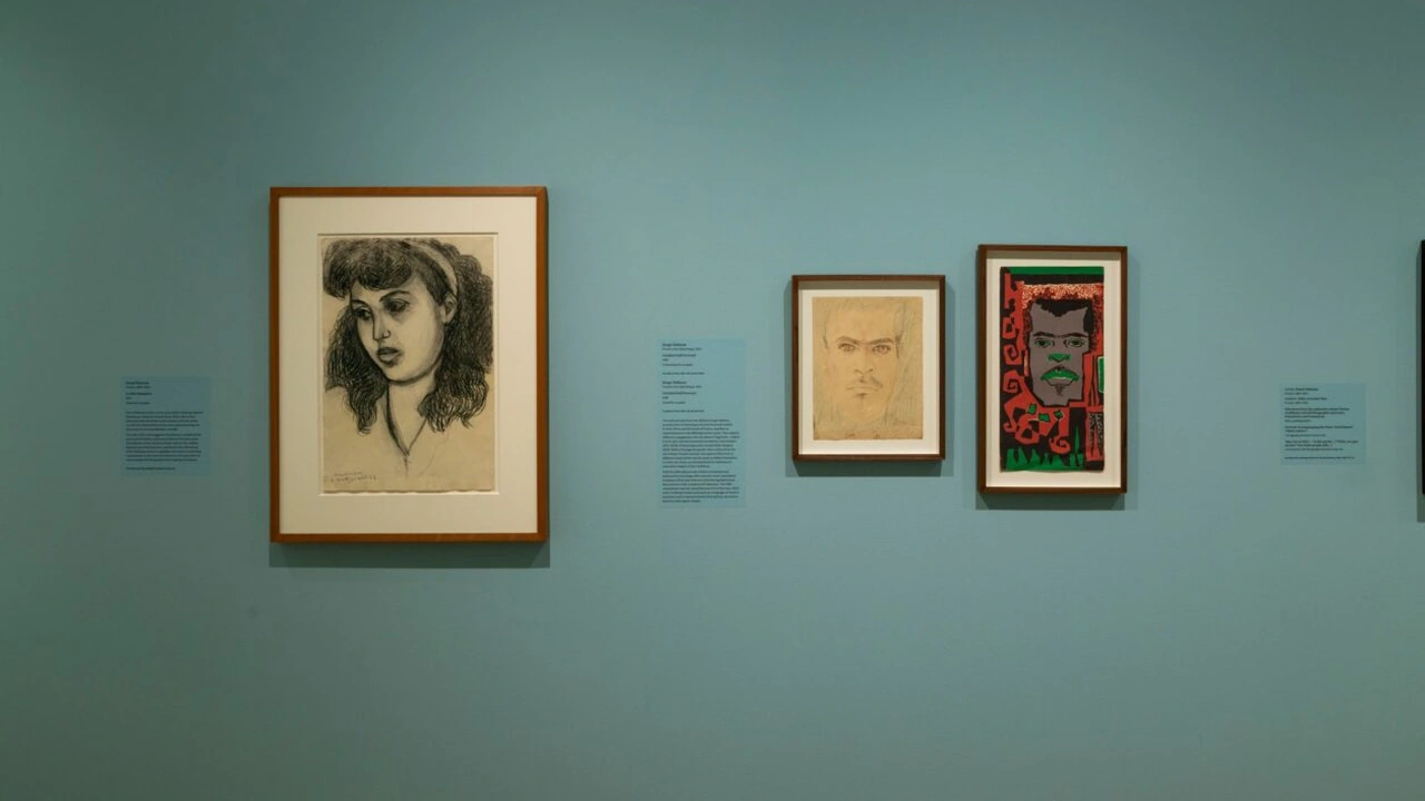 Three framed portraits hang on a teal gallery wall with small labels between them.