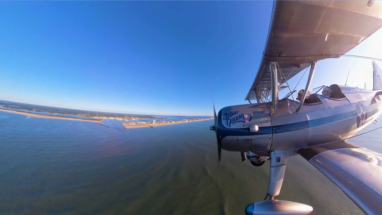 A vintage biplane flies over the water