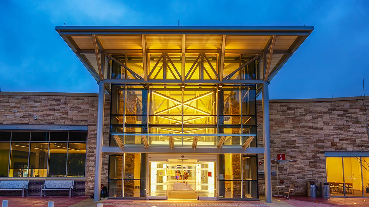 A glass and stone building entrance glowing with light at dusk
