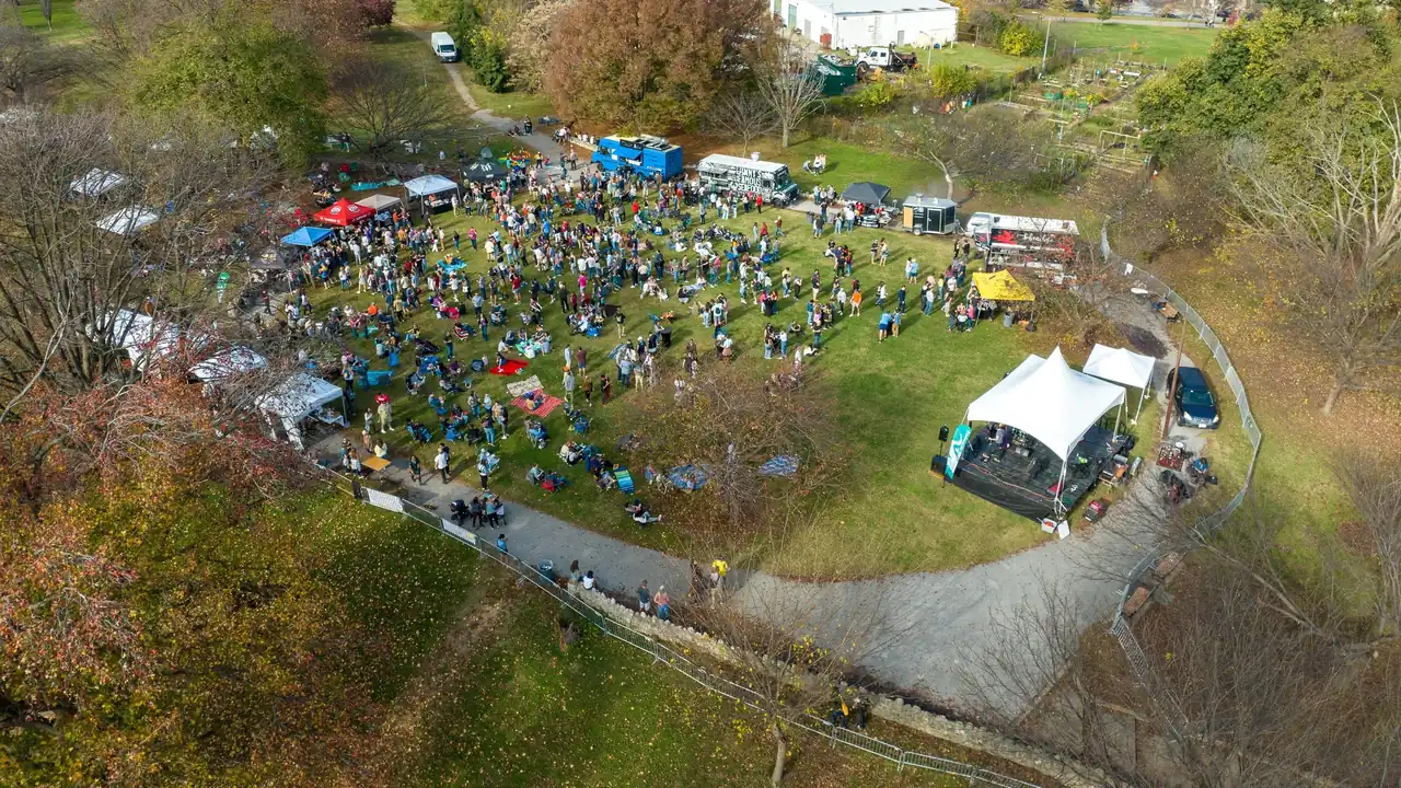 Aerial view of a crowd and white tents in a green park surrounded by fall trees.