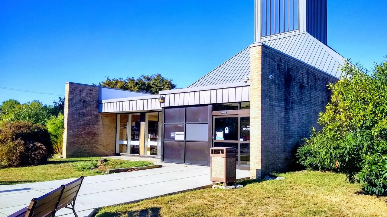 A modern brick building with a tall angled roof against a bright blue sky.