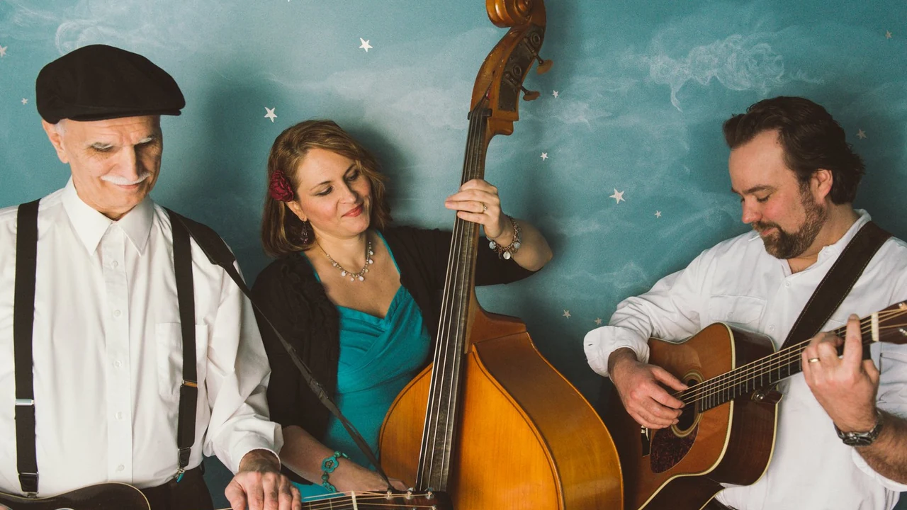 Three musicians with a bass, guitar and flat caps pose against a teal backdrop.