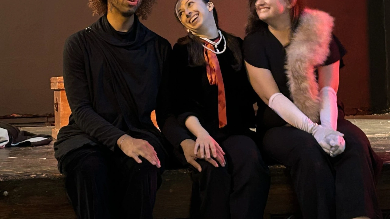 Three performers sit together onstage