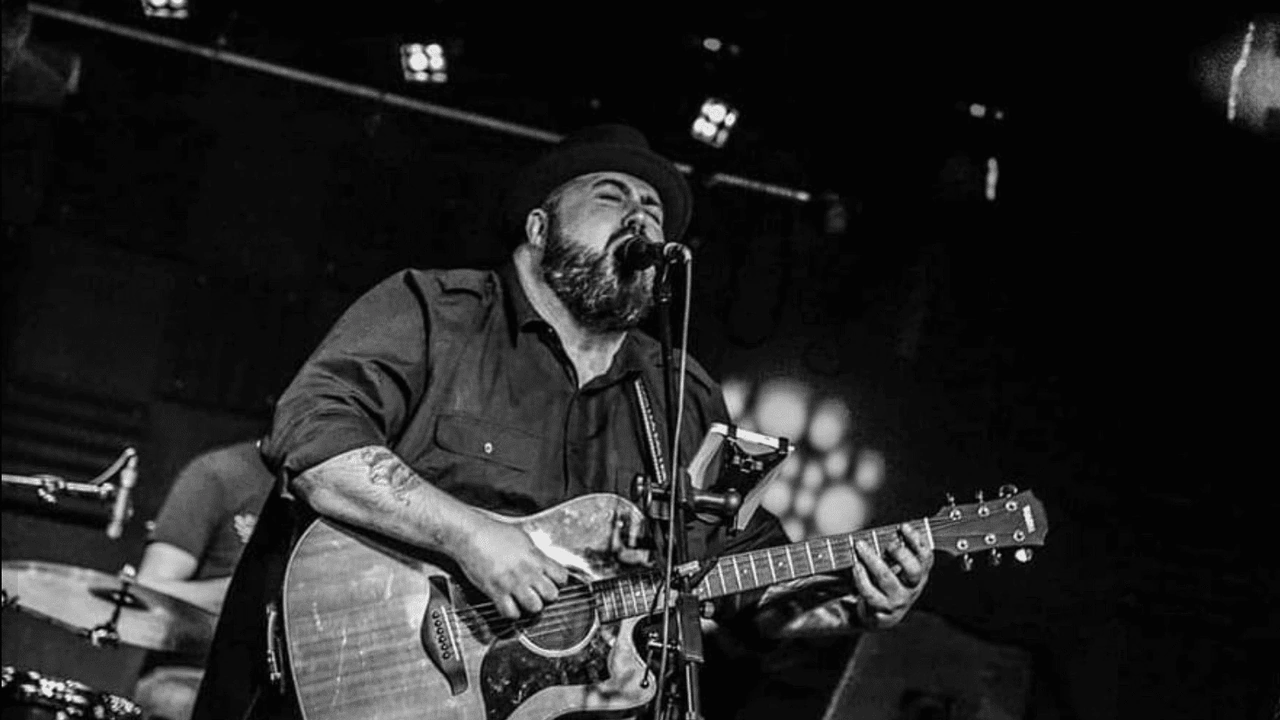 A bearded guitarist sings in black and white
