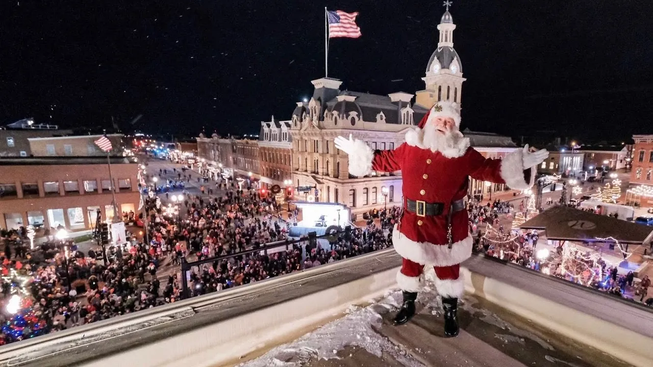 Santa waving from a rooftop above a crowded, lit-up downtown street at night.
