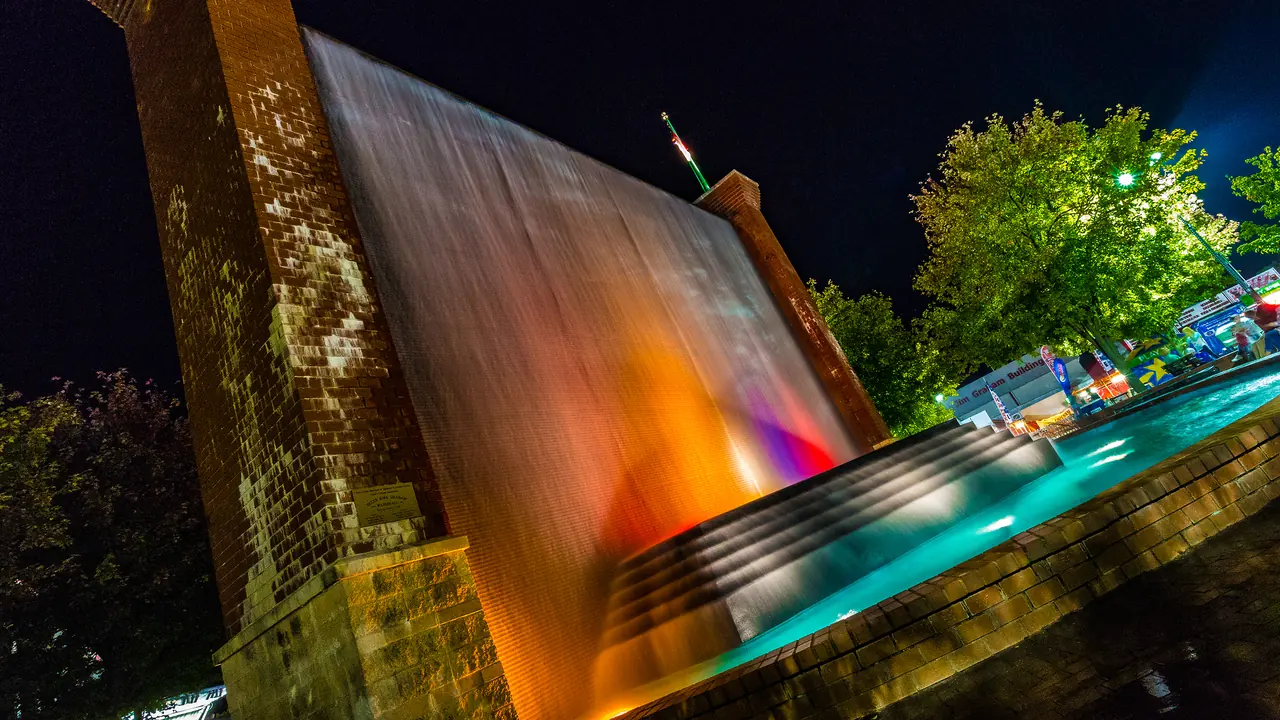 A lit fountain glows beside a pool at night