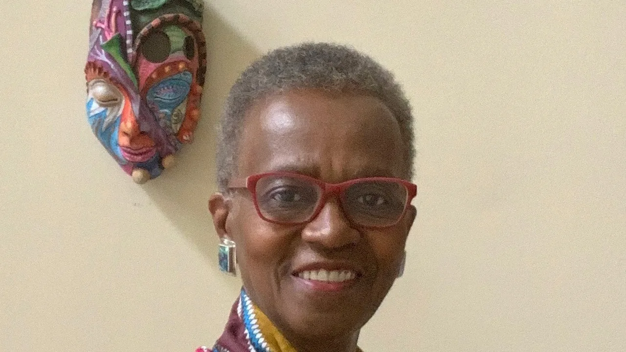 A smiling woman in red glasses beside a carved mask