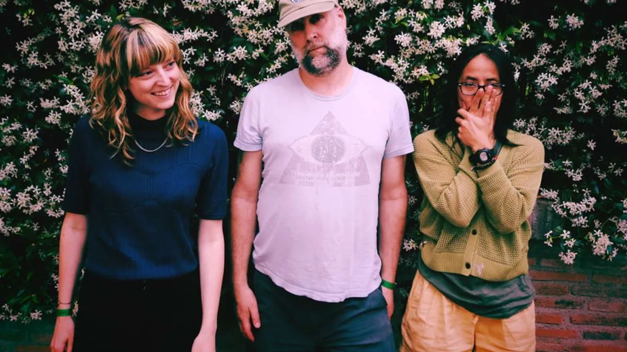 Three musicians pose before a flowering hedge