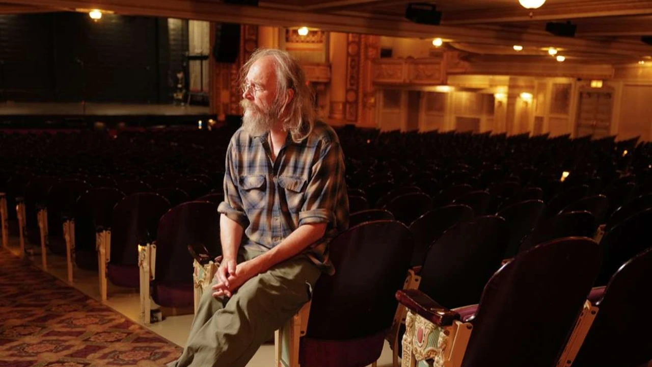 A musician sits among the seats of an ornate theater