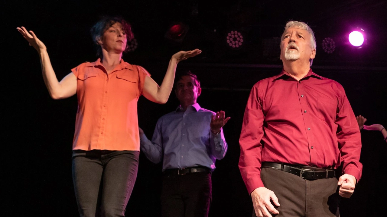 Three improv actors gesture mid-scene on a dark stage under colored lights.
