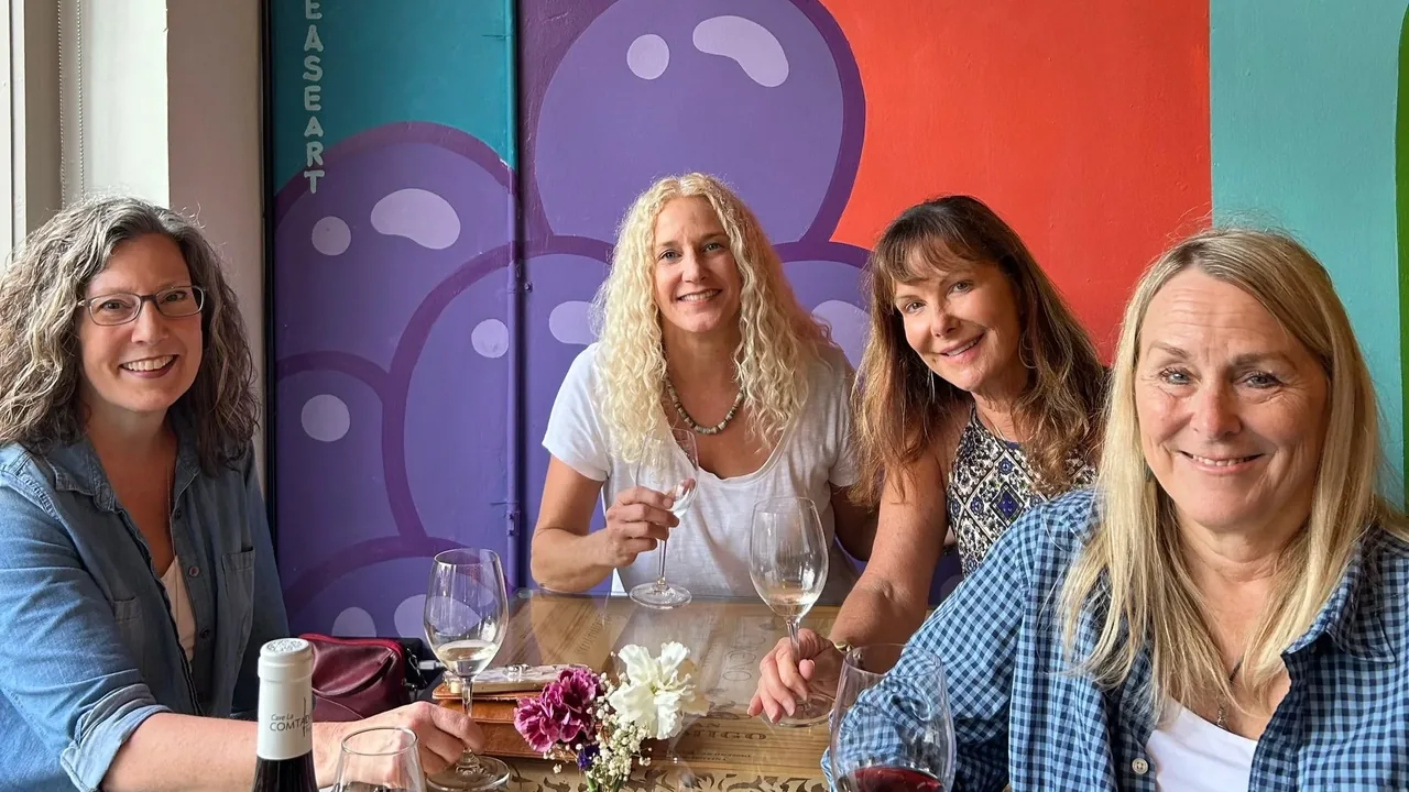 Four women laugh together over wine