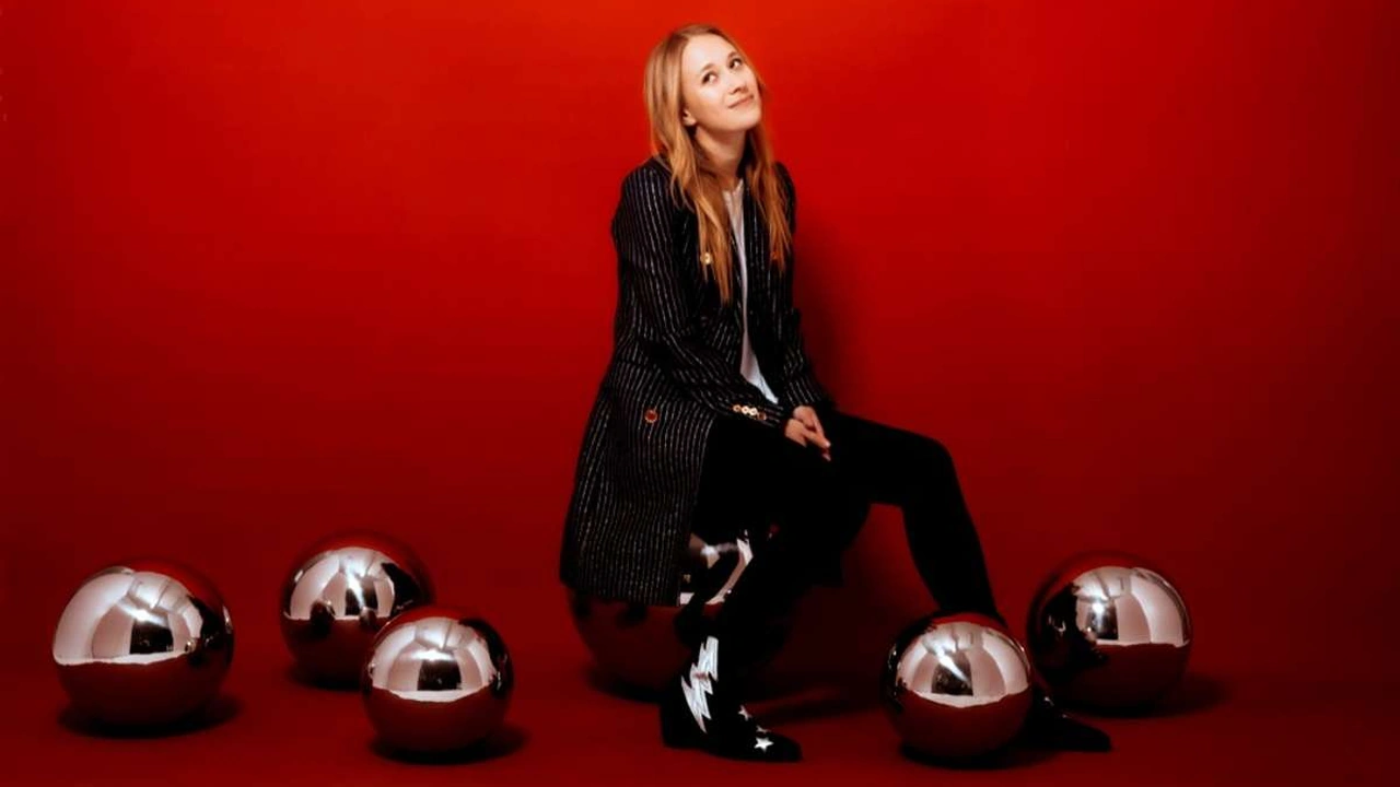 A singer sits against a red backdrop with silver spheres