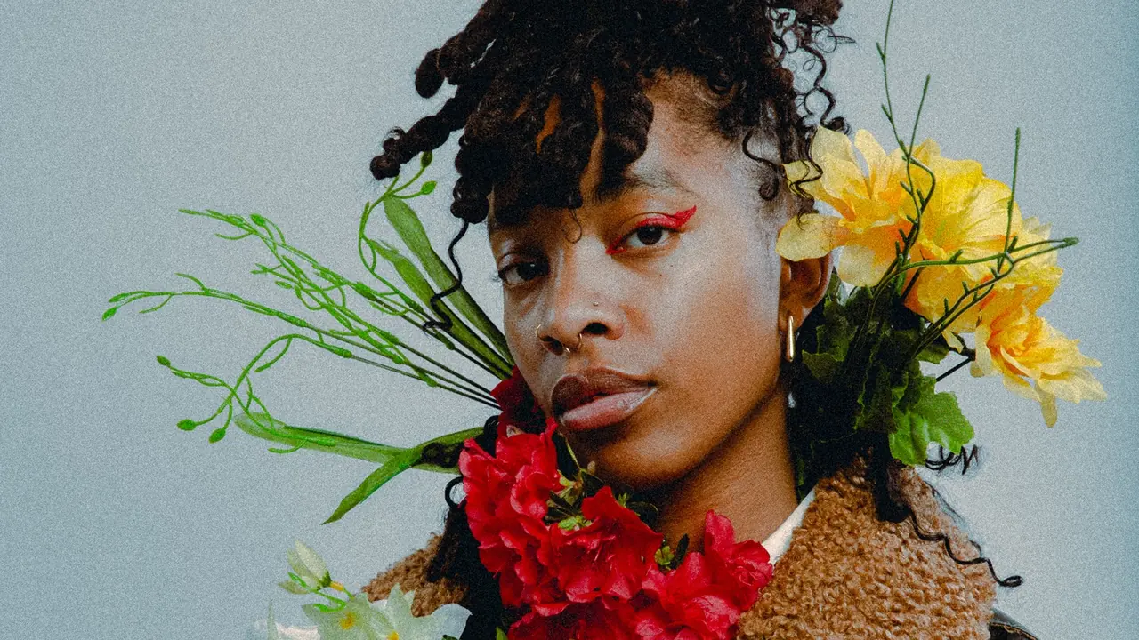 A woman framed by bright flowers looks at the camera