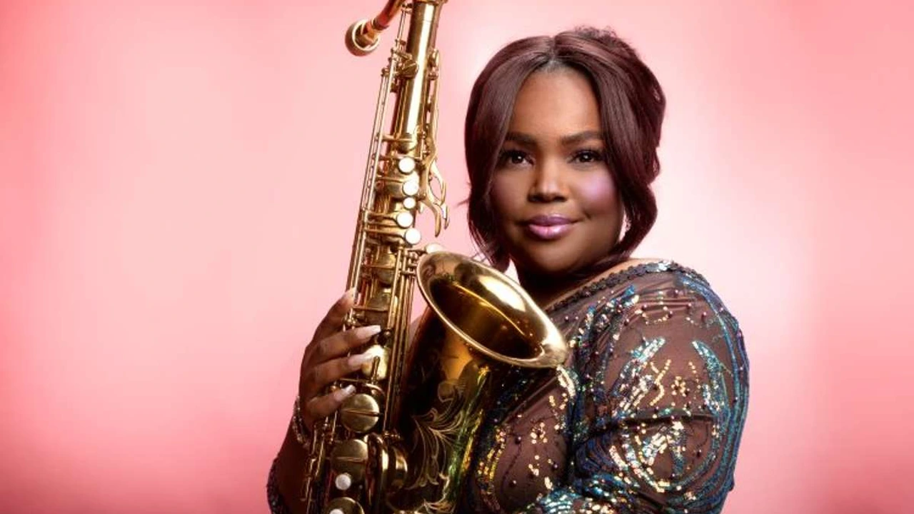 A saxophonist poses against a pink backdrop
