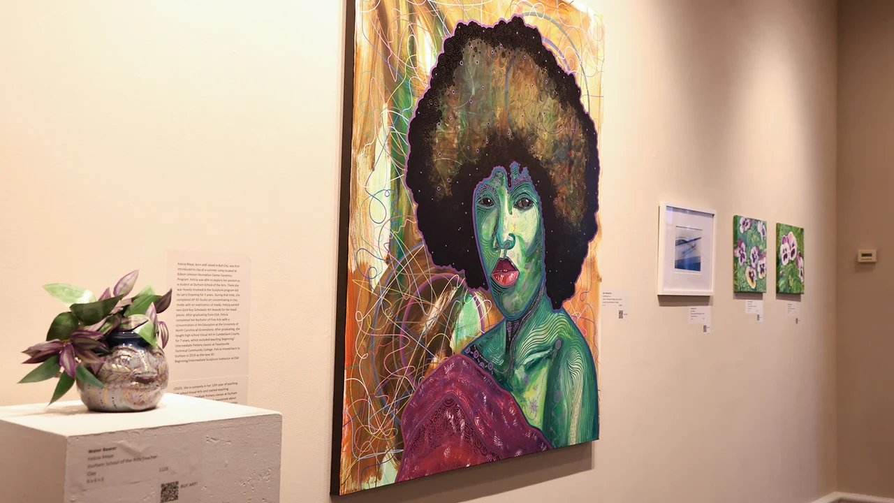 A gallery wall with a large colorful portrait painting and small framed works, with a plant on a pedestal.
