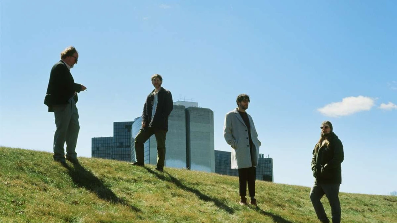 Four musicians stand on a grassy hill