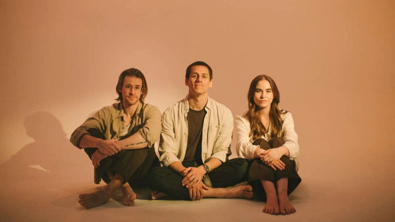 Three musicians sit together against a warm backdrop