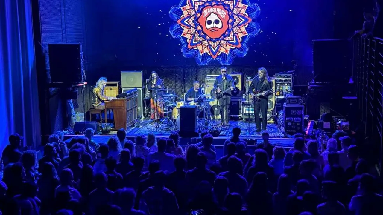 A band plays to a packed hall under blue lights