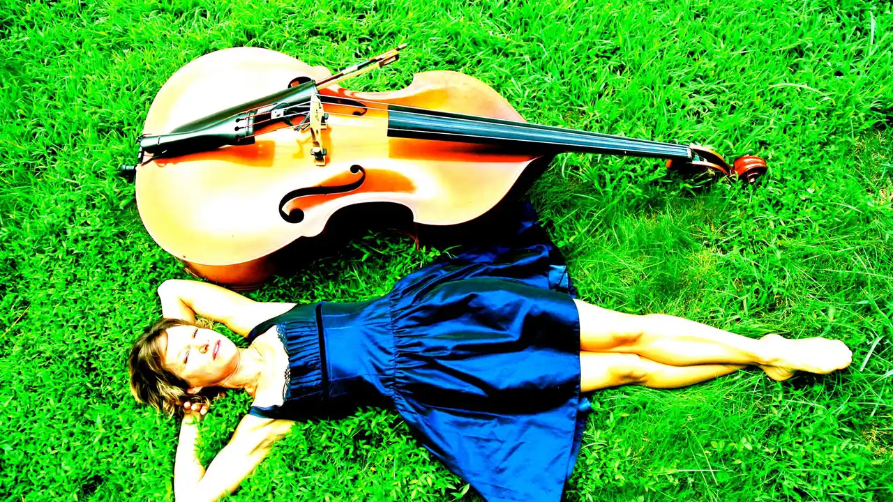 A woman lies on the grass beside a cello
