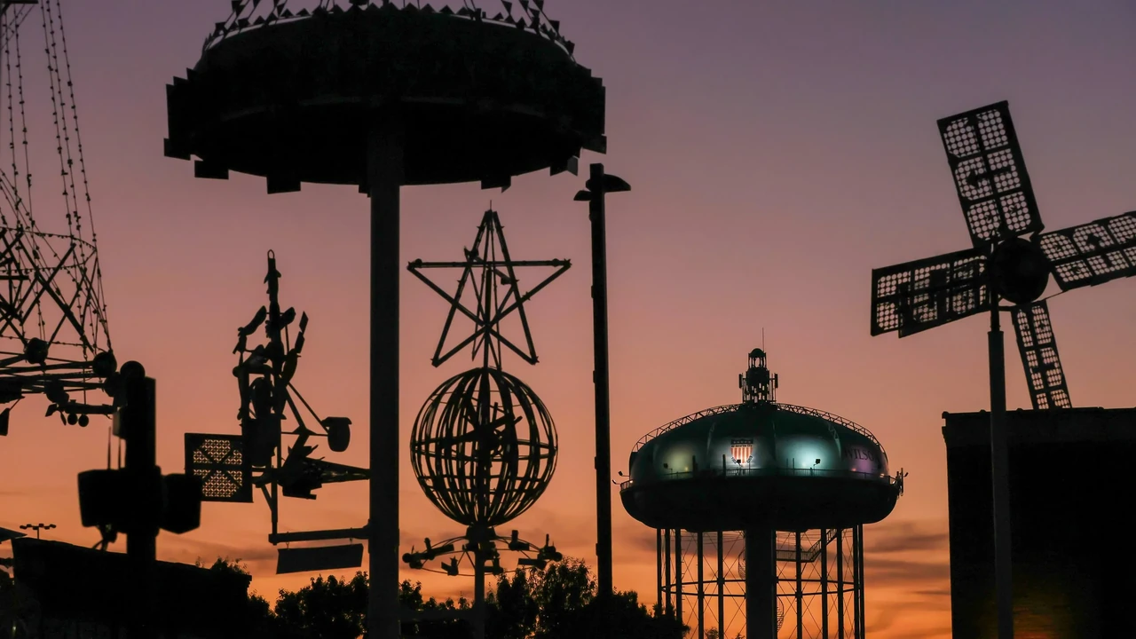 Silhouettes of a water tower, a windmill and metal sculptures against an orange sunset.
