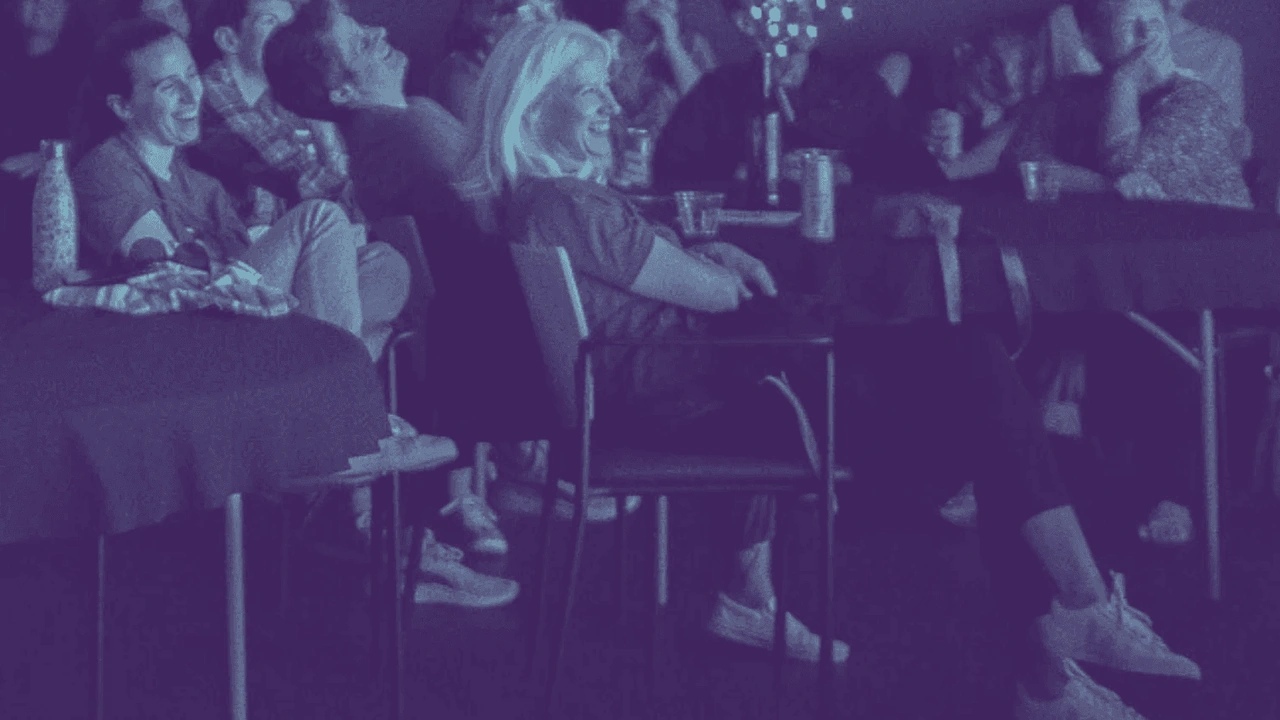 An audience laughs in a dim theater