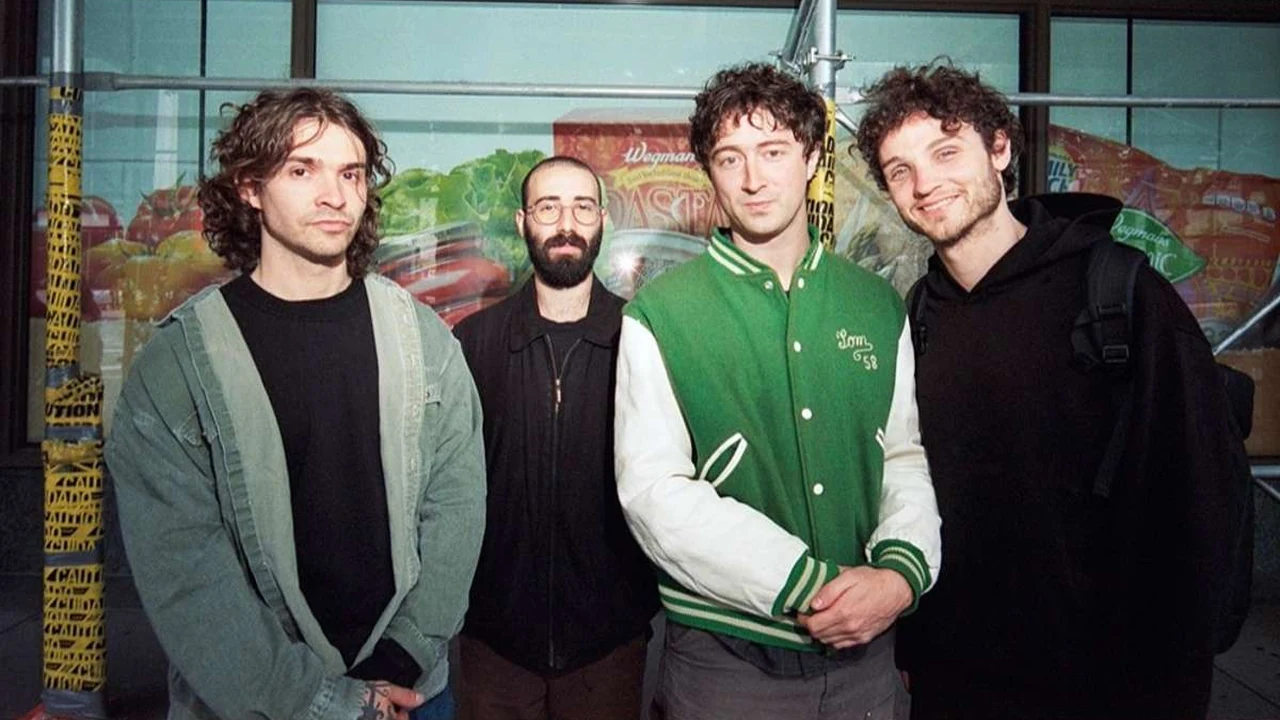 Four young musicians pose together in front of a colorful mural.