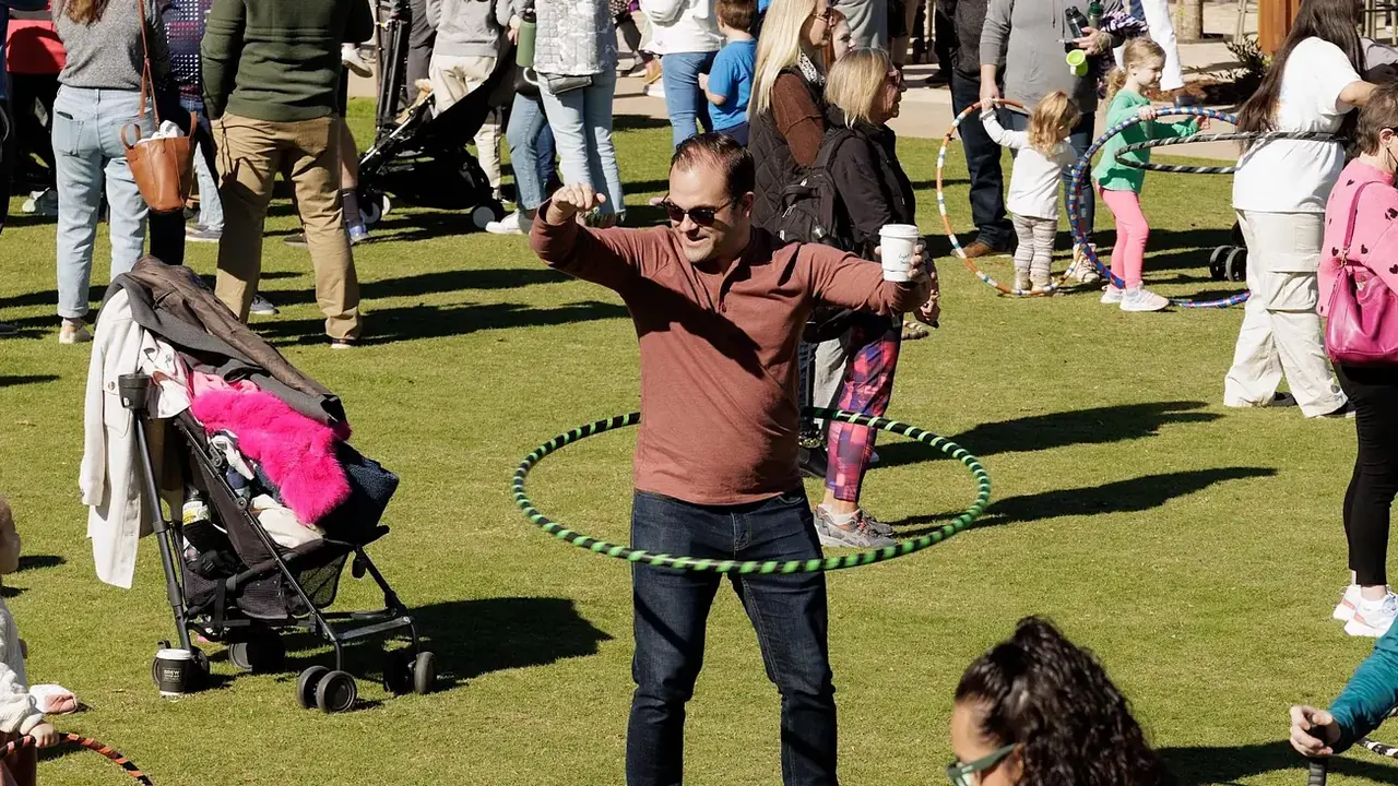 Families play with hula hoops on a park lawn