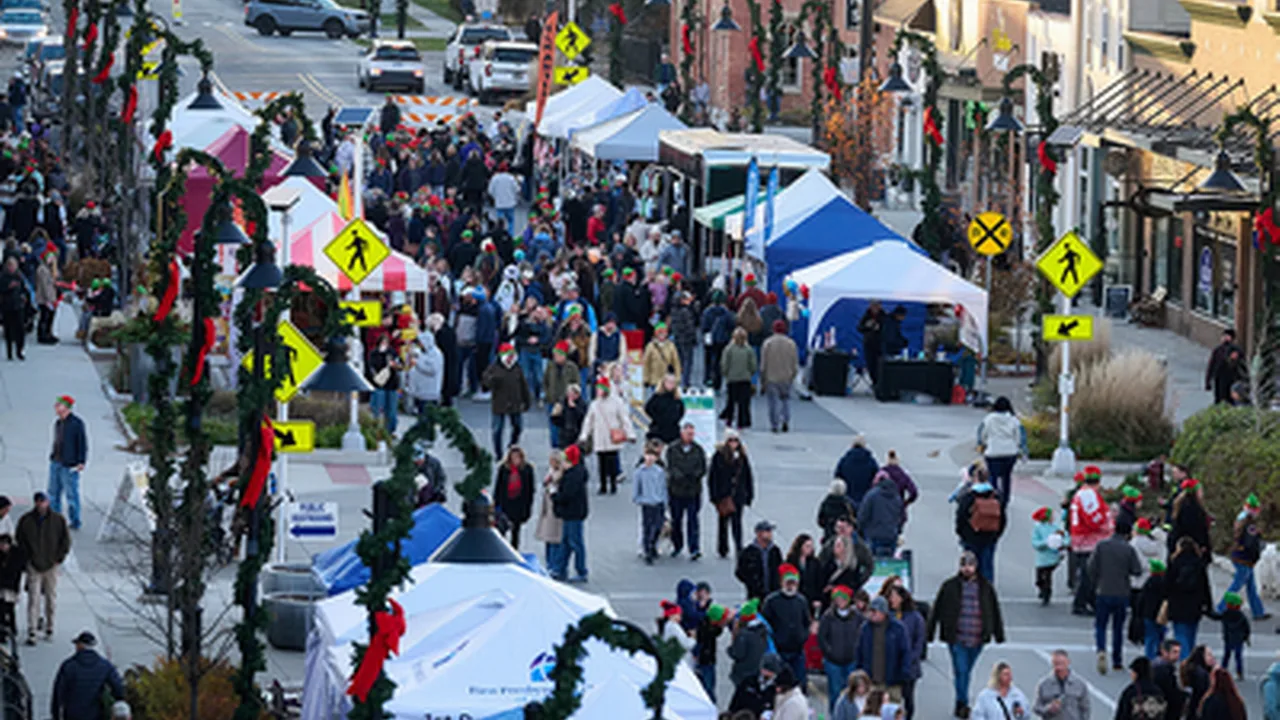 A crowded downtown street lined with white vendor tents and garland-wrapped lampposts.