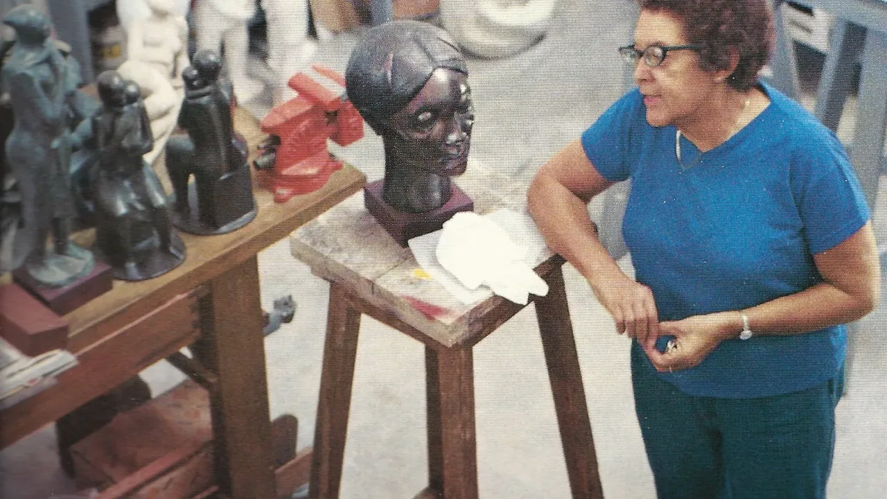 A woman examines carved sculptures and busts at an outdoor table