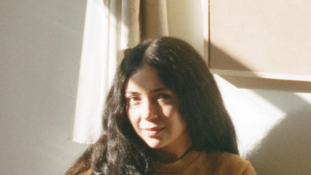 A young woman with long dark hair smiles in soft window light