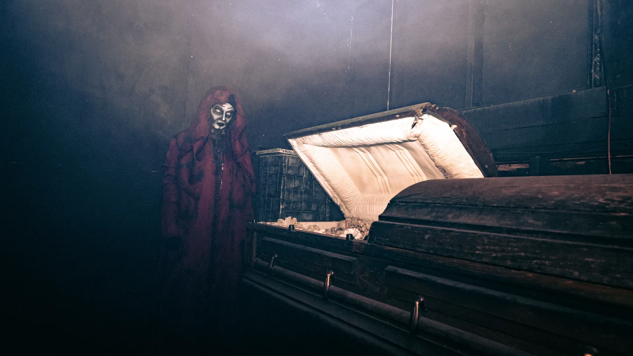 A masked ghoul looms beside an open coffin in a dark haunted room